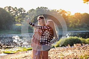 Two sisters, younger and older, take a selfie in the summer on a smartphone against the backdrop of beautiful nature