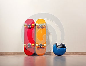 Two skateboards, yellow and red, are standing against the wall, a blue protective helmet is lying next to it, the floor is wooden