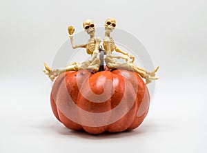 Two skeletons sitting on top of a Halloween pumpkin  on white