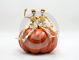 Two skeletons sitting on top of a Halloween pumpkin  on white