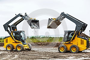 Two skid steers with raiced bucket outdoors