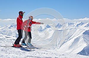 Two skiers are on edge of a cliff in mountains