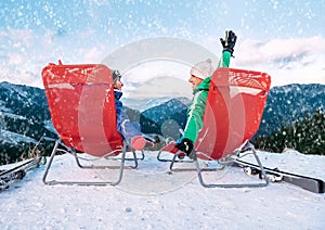 Two skiers relax in chiars on the mountain top