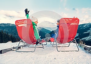 Two skiers relax in chiars on the mountain top