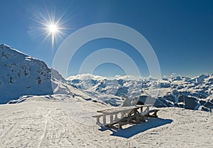 Two skiers sat at picnic table relaxing on piste