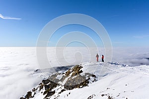 Two skiers on top of mountain above the clouds