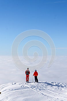 Two skiers on top of mountain above the clouds