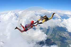 Two skydivers in color suits are falling above white clouds.