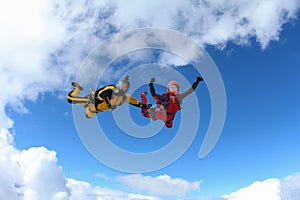 Two skydivers in color suits are falling in the clouds.