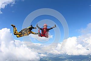 Two skydivers in color suits are falling in the clouds.