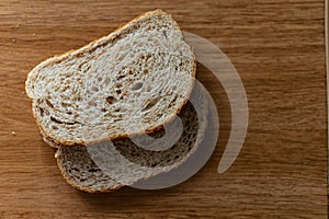 Two sliced slices of bran bread with a crisp crust of rye flour, lying on a brown wooden table, after fresh baking