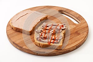 Two slices of bread coated with pate and ketchup on wooden board