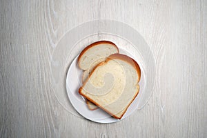 Two slices of bread on white plate on white wooden verneer background
