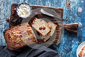 Two slices cut from a cranberry rosemary quick bread on a wooden board served with cream cheese.