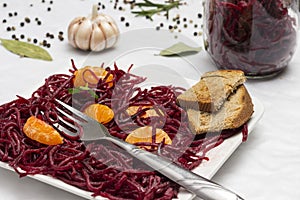 Two slices of mandarin on sliced fermented beets and fork in plate. Glass jar with beets. Garlic