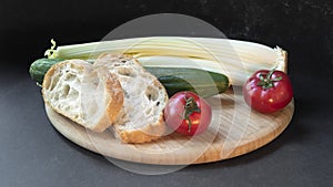 Two slices of white beautiful airy white bread, fresh vegetables - cucumbers, tomatoes and celery, all on a round wooden cutting