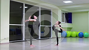 Two slim girls sisters artistic gymnasts in black sportswear do warm-up and perform exercises in rhythmic gymnastics in gym