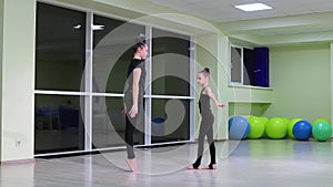 Two slim girls sisters artistic gymnasts in black sportswear do warm-up and perform exercises in rhythmic gymnastics in gym