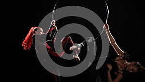 Two slim woman in shiny costumes spinning air hoop doing arabesque trick simultaneously. Wide shot of Caucasian aerial