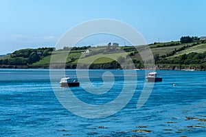 Two small boats are anchored in Clonakilty Bay on a sunny spring day. Beautiful Irish seaside landscape. Clear sky and blue water