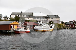 Two small boats at Reine harbor in front of traditional wooden fishing cabins on Lofoten Islands in Norway.