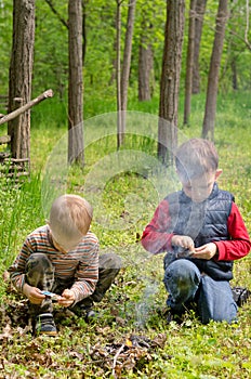 Two small boys lighting a fire in woodland