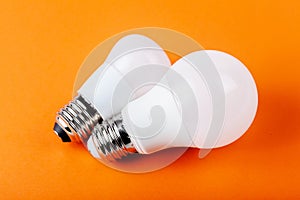 Two small bright white energy saving bulbs. Pair of modern eco lightbulbs laying isolated on orange background. Power saving