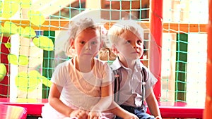 Two small child sit on trampoline and bounce.