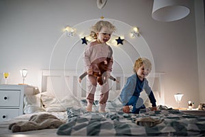 Two small children jumping on bed indoors at home, having fun.