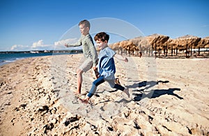 Two small children running outdoors on sand beach.