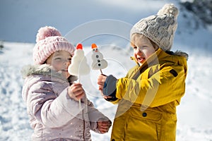 Dve malé deti stojace v snehu v zimnej prírode, jedia sladkosti.