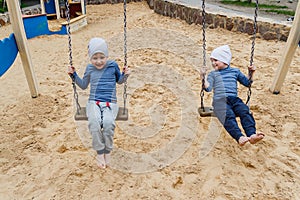 Two small children swing on the swing outdoors