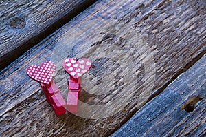 Two small clothespins hearts lie on a wooden table. Love