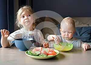 Two kids eating soup and vegetables for lunch at home