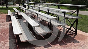 two small empty outdoor sports silver bleacher sets with cars passing on road