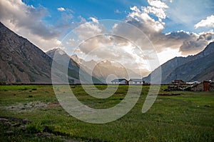 Two small farm houses in lush green valley surrounded by high mountains during sunrise