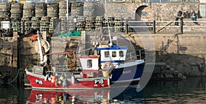 Two small fishing boats, one red and one blue moored by jetty in Brixham Harbour