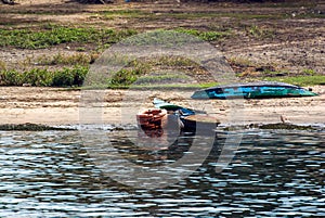 Two small fishing boats, typical of the Nile river, one on the shore of the river and the other on dry land with the keel up. Both