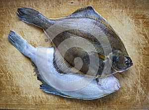 Two small flounders lie diagonally on a wooden board. Cooking a fish dish