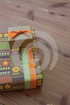 Two small gift boxes in green orange and brown with ribbons, retro style, neutral wood background