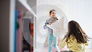 Two small girls sisters indoors at home, pillow fight in bedroom.