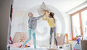 Two small girls sisters indoors at home, pillow fight in bedroom.