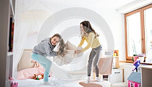 Two small girls sisters indoors at home, pillow fight in bedroom.