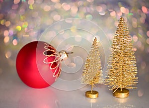 Two small gold Christmas tree and red christmas ball on a glass surface with defocused background with bokeh lights.