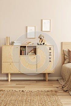 Two small graphics in wooden frames on empty wall of stylish interior with wooden cabinet