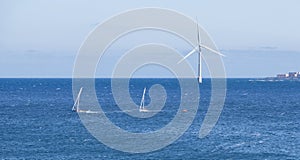 Two small lateen sailboats sail near an offshore wind turbine on the island of Gran Canaria