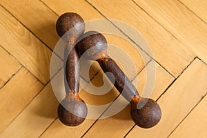 Two small old rusty dumbbells lie on a wooden floor. View from above