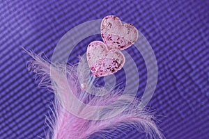 Two small pink fabric hearts on a white plastic stick with feathers