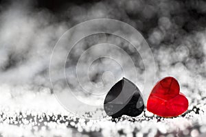 Two small red and black plastic hearts lying next to each other with beautiful silver bokeh effects and a copy space for text.