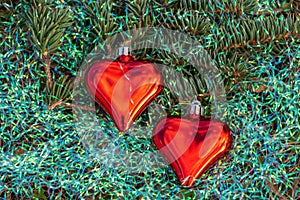Two small red glass hearts with colorful rainbow Christmas decorations and a small green fir tree branch